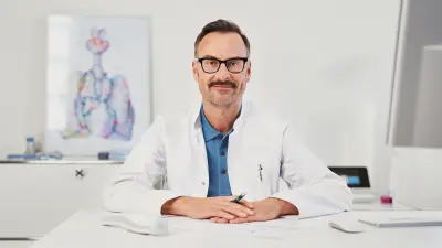 Confident-looking doctor sitting at desk in doctor's office environment with Vivatmo pro in background