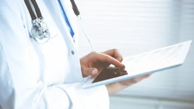 Nahaufnahme von Arzt mit Stethoskop um den Hals, in den Händen ein Tablet haltend.